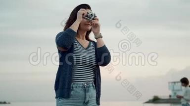 年轻女子在海边的老式相机上拍照。 一个有复古相机的女孩的肖像